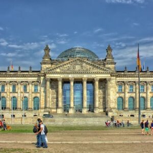 Front view of the Reichstag Building in Berlin with people and flags, under a bright sky.
