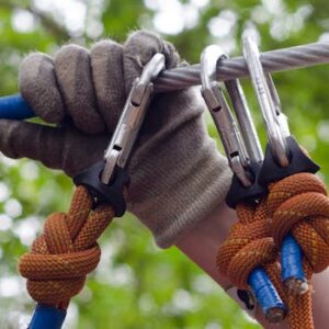 Close-up of a climber's gloved hand securing carabiners on a cable, showcasing outdoor activity gear.