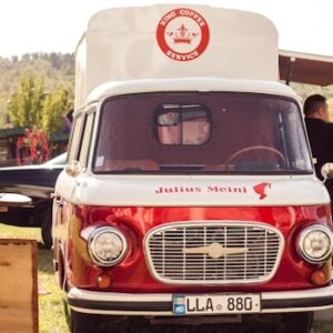 Red and white vintage coffee truck serving at an outdoor event on a sunny day.