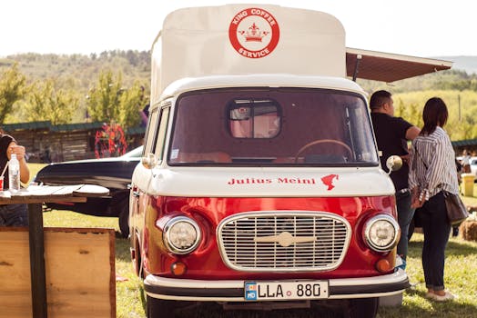 Red and white vintage coffee truck serving at an outdoor event on a sunny day.