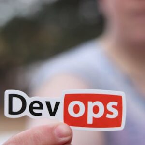 A close-up image featuring a DevOps sticker held by a person outdoors.