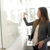 Professional woman writing on a whiteboard in an office environment, focusing on ideas.