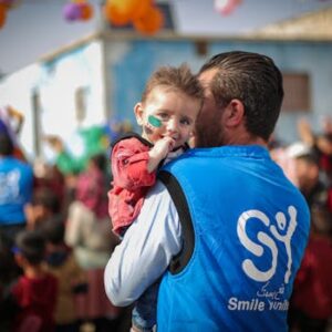 A volunteer holds a toddler during a charity event in Idlib, Syria, symbolizing hope and community.