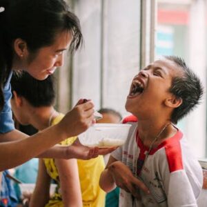 Joyful moment as a woman feeds a happy child in a warm, indoor setting.