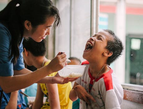 Joyful moment as a woman feeds a happy child in a warm, indoor setting.