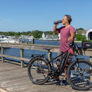 Man standing on a boardwalk in Patchogue, NY, enjoying a view while drinking next to an e-bike.