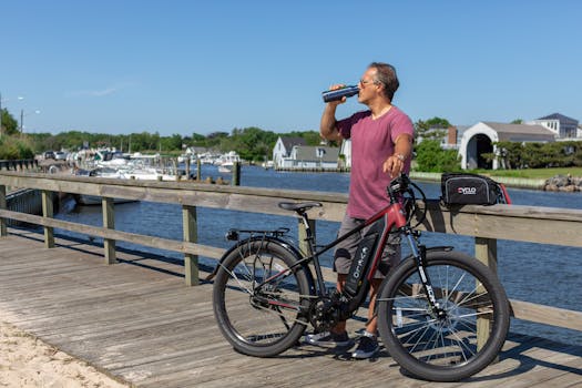 Man standing on a boardwalk in Patchogue, NY, enjoying a view while drinking next to an e-bike.