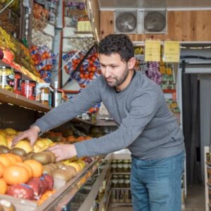 Grocery store worker organizing fresh fruits and vegetables on display shelves.