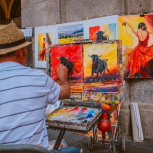 Street artist painting vibrant bull and flamenco dancer scenes in an outdoor market.