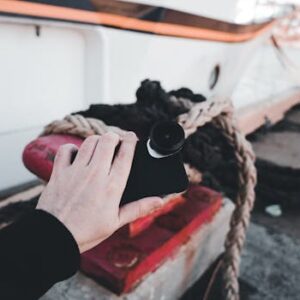 A hand holding a smartphone with fisheye lens by the harbor, showcasing technology and travel.