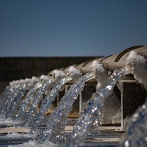 Close-up view of water flowing from industrial pipes against a clear blue sky.