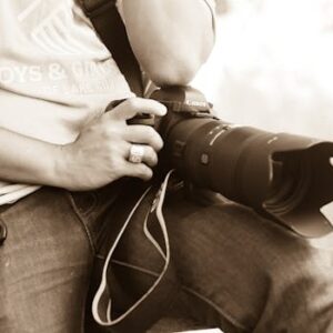 Close-up of a photographer sitting with DSLR camera outdoors, holding keys.