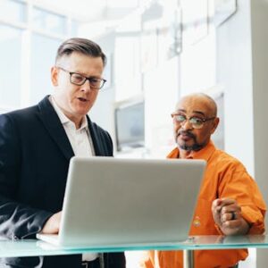 Two business professionals engaged in a collaborative discussion over a laptop in a modern office setting.
