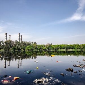 View of a polluted river reflecting factory emissions under a clear sky in India.