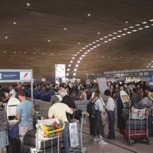 Crowded airport terminal with travellers in line. Indoor setting with modern architecture.