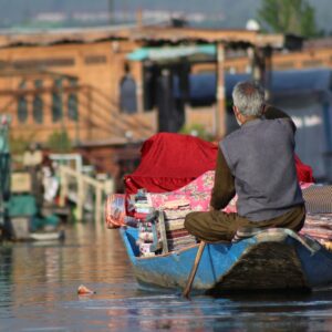 Senior man paddles a boat loaded with goods on a charming urban river, showcasing daily life and transportation.
