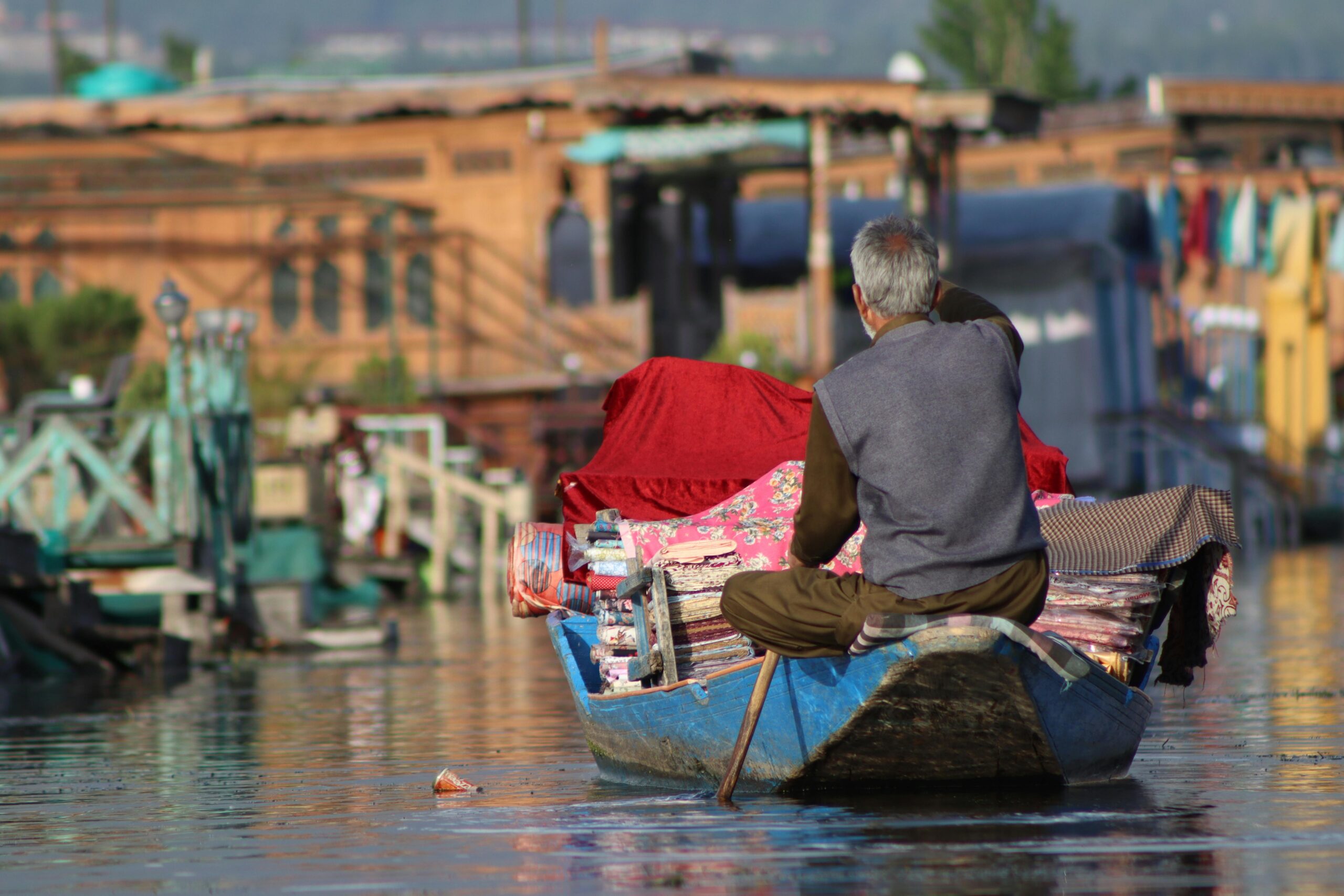 Senior man paddles a boat loaded with goods on a charming urban river, showcasing daily life and transportation.