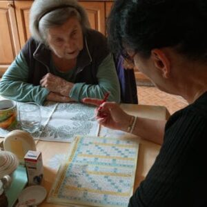 A senior woman and her caregiver work together on a crossword puzzle in a cozy kitchen.