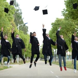 A joyful group of graduates throwing caps in the air during a graduation ceremony in a park setting.