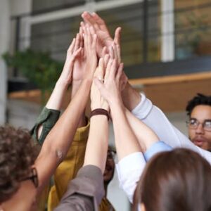A group of diverse professionals celebrating teamwork with a high-five indoors.