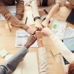 Top view of a diverse team fist bumping over a meeting table with paperwork and laptops, symbolizing teamwork.