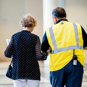 A security officer helps an elderly woman inside a modern building hallway.