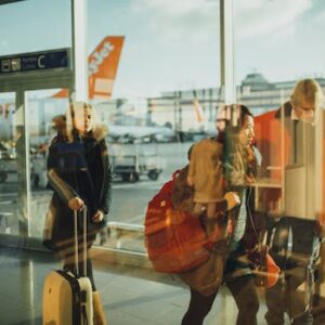 Passengers moving through an airport gate area with visible airplanes outside.
