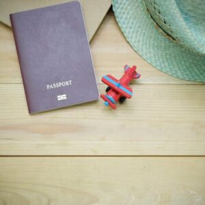 Flat lay of a passport, straw hat, and toy airplane on a wooden surface.