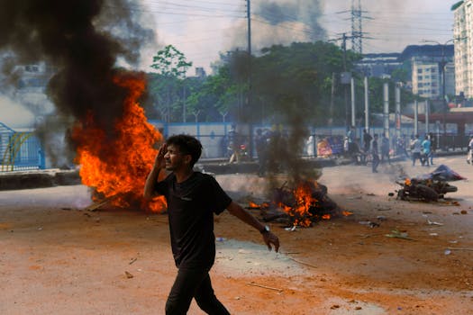 A man walks past burning debris during an outdoor protest in a city, reflecting tension and unrest.