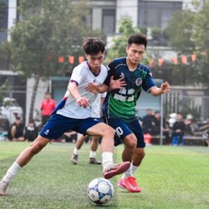 Two soccer players in action during a match on a lush green turf field in Hà Nội.