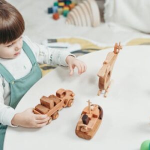 A young child playing with wooden toys at a round table in a bright playroom.