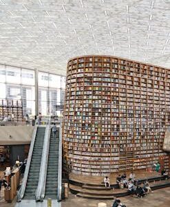 Interior view of a modern library in Seoul with a vast bookshelf and escalators under a glass ceiling.