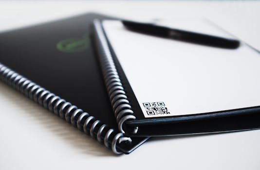 Close-up of spiral notebooks showing a QR code and blurred pen.