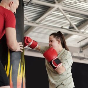 A woman with Down syndrome energetically trains boxing with a coach in a gym setting.