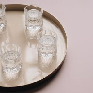 Five crystal glasses filled with water arranged on a round beige tray, creating a minimalist reflection.