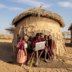 Group of African children in a Tanzanian village using a laptop outdoors, engaged in learning.