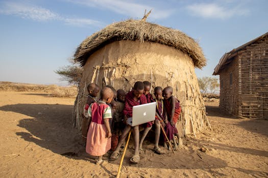 Group of African children in a Tanzanian village using a laptop outdoors, engaged in learning.