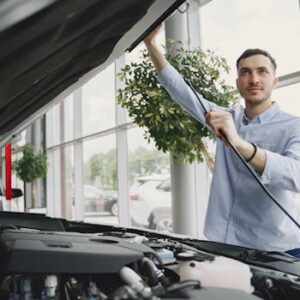 A man carefully checking a car engine in a bright, modern car showroom.