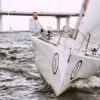 Experience the thrill of sailing with a yachtsman navigating a vessel under a striking bridge.