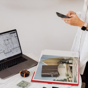 Stylish person with a smartphone at work desk with laptop and charts.