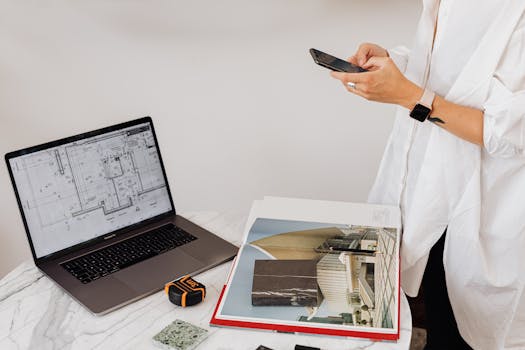 Stylish person with a smartphone at work desk with laptop and charts.