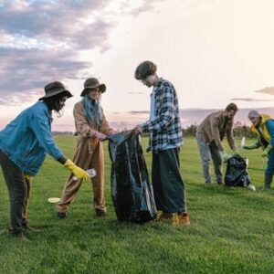 A diverse group of volunteers collecting trash in a field at sunset, promoting environmental awareness.