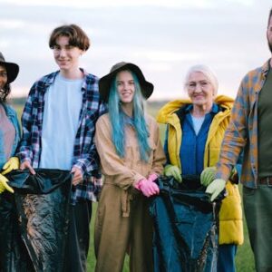 Group of smiling volunteers cleaning a green field, holding plastic bags. Diverse team promoting environmental care.