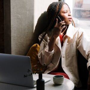 Woman with braids talking on phone in a cafe, sunlight through window.