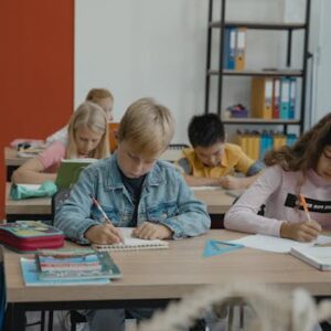 A group of children studiously engaged in writing and learning in a vibrant classroom setting.