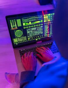 An unrecognizable person using a laptop indoors with digital screens displaying data and analytics.