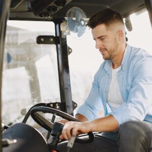A young man is focused on driving a modern tractor with precision. The sunlight highlights the indoor setting.