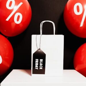 White shopping bag with Black Friday tag surrounded by red discount balloons.