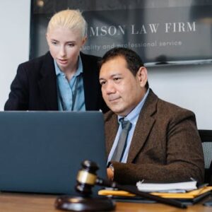 Smart mature ethnic judge in suit working on laptop and discussing details of new case with young female assistant in law firm
