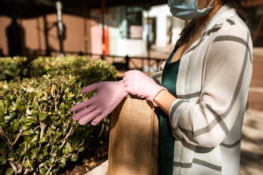 Individual outdoors adjusting a face mask while wearing pink gloves and a checkered shirt.